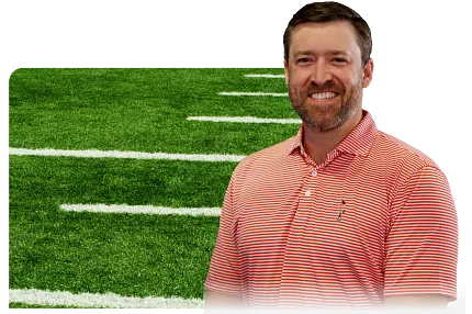 Man in red striped shirt smiling in front of synthetic turf football field background. Man in red striped shirt smiling in front of synthetic turf football field background.