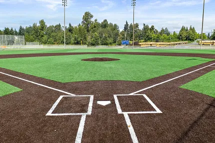 Artificial Turf Baseball Field with Brown Infield and Green Outfield Artificial turf baseball field with brown infield and green outfield under a clear blue sky