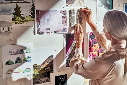Senior Interior Designer Selecting Carpet Swatches for Project Elderly woman pinning carpet swatches on a mood board with various landscape and architectural images