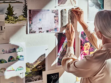 Senior Interior Designer Selecting Carpet Swatches for Project Elderly woman pinning carpet swatches on a mood board with various landscape and architectural images