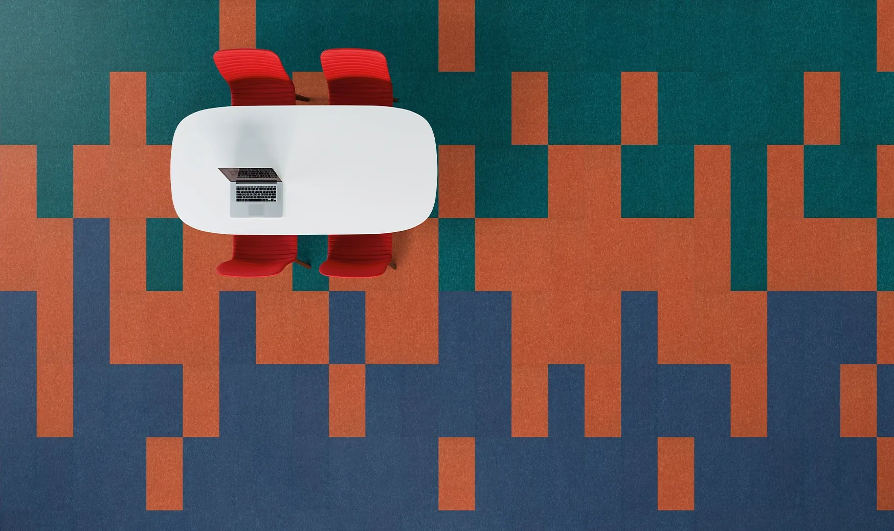 Overhead view of a modern office space with a colorful geometric pattern carpet in teal, orange, and blue, featuring a white oval table and two red chairs