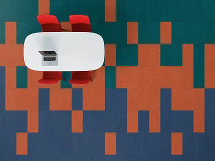 Modern Office Space with Geometric Pattern Carpet in Teal, Orange, and Blue Overhead view of a modern office space with a colorful geometric pattern carpet in teal, orange, and blue, featuring a white oval table and two red chairs