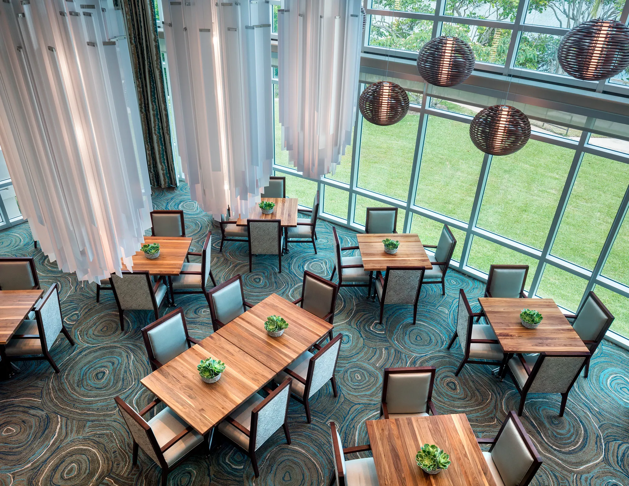 Aerial view of a senior living dining area with modern wooden tables, cushioned chairs, and intricate patterned commercial carpet tile flooring