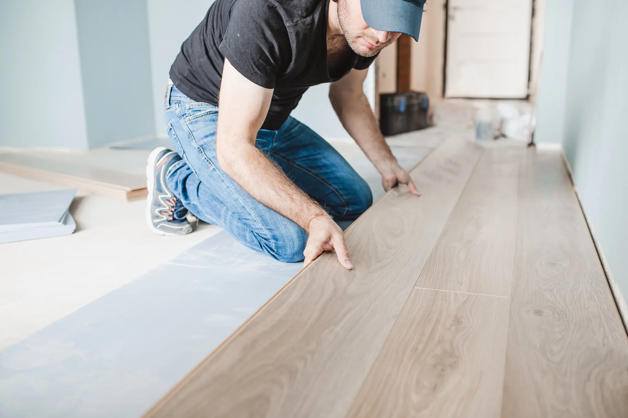 Man installing light wood flooring in a room