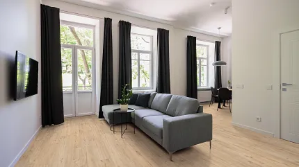 Contemporary Living Room with Durable Light Wood Laminate Flooring Modern living room with light wood laminate flooring, gray sectional sofa, and black curtains