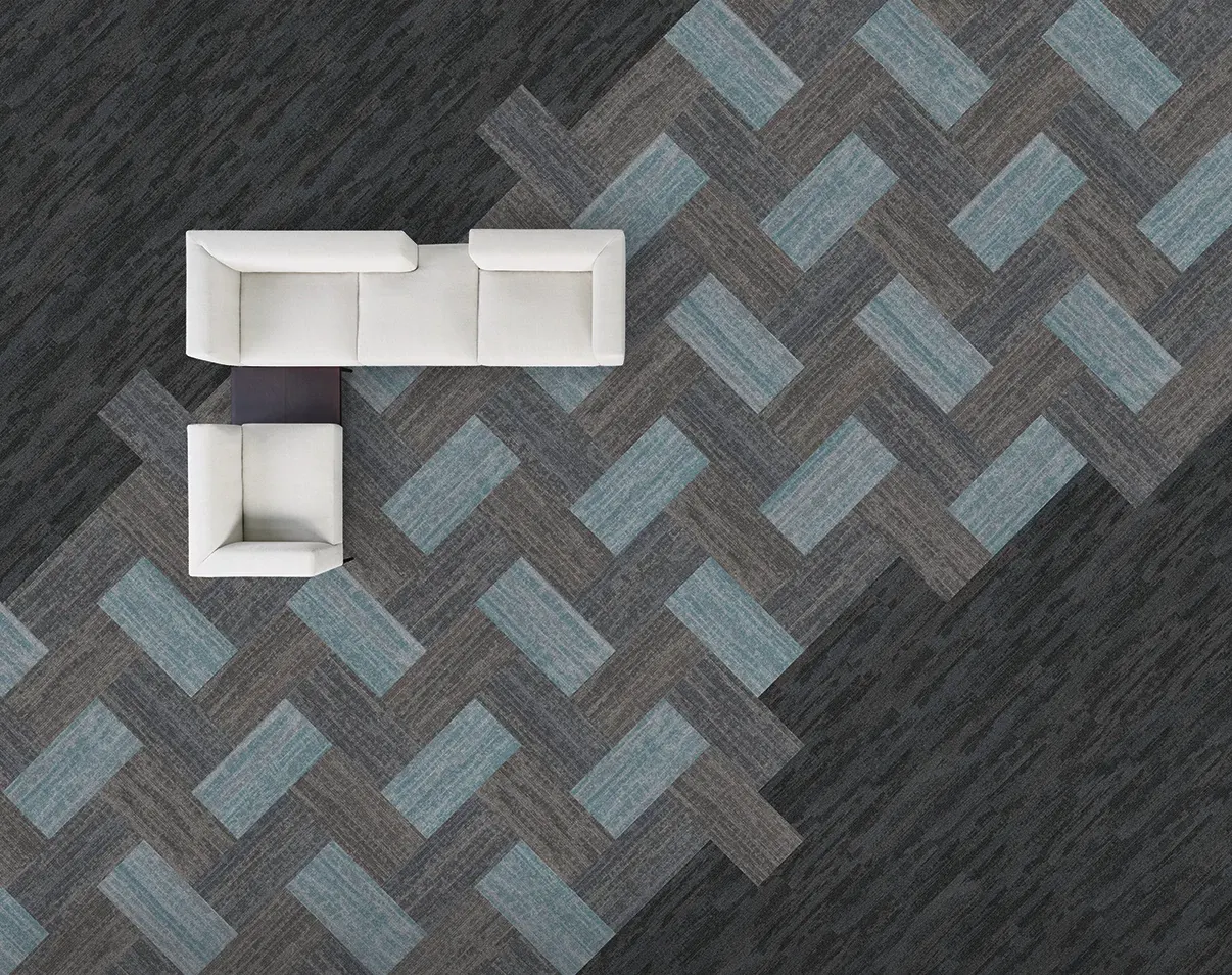 Overhead view of a modern office space featuring a white sectional sofa on a patterned commercial carpet tile floor in shades of blue, gray, and charcoal