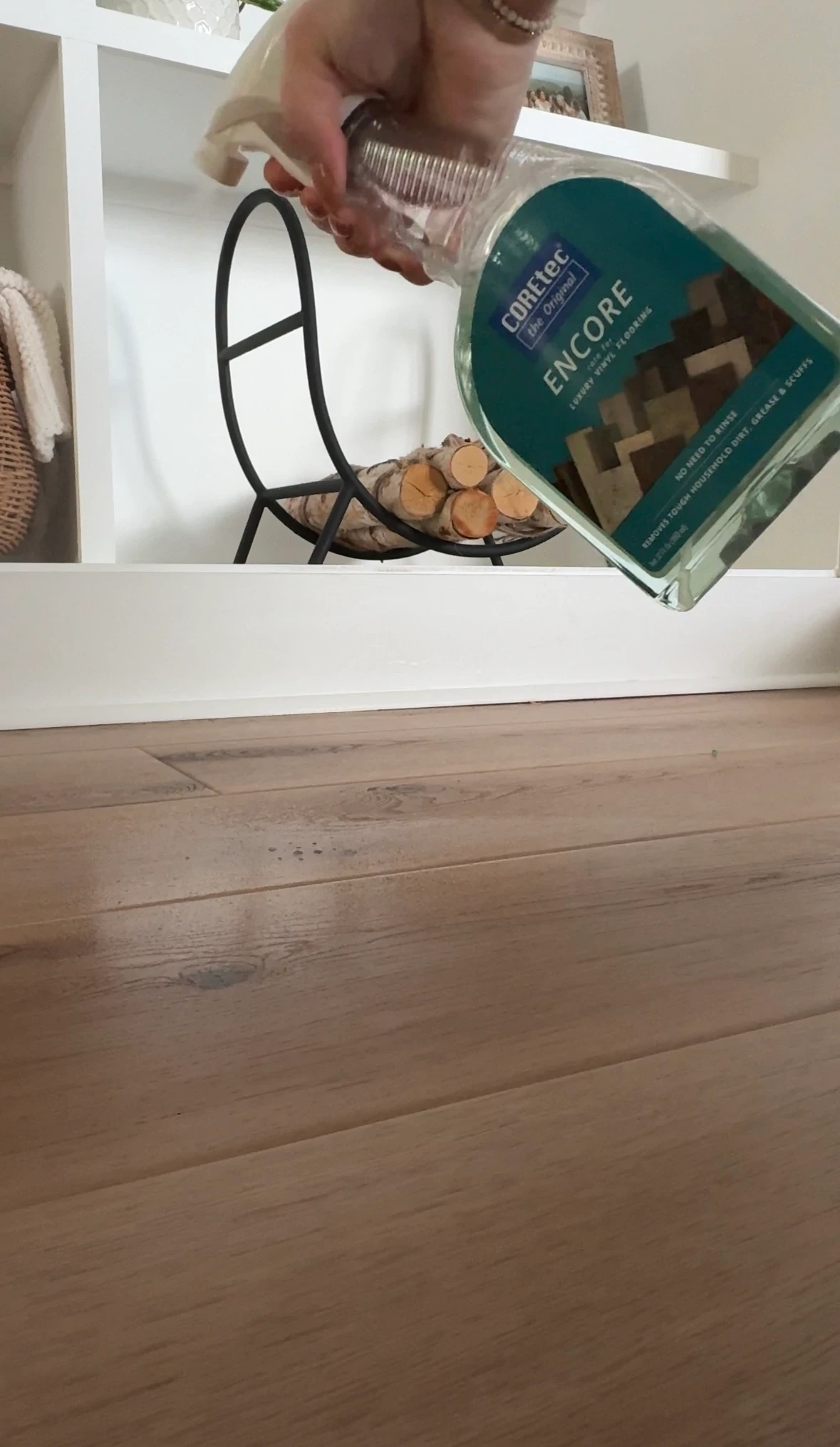 Hand holding COREtec Encore floor cleaner bottle over wood look vinyl flooring in a cozy living room setting