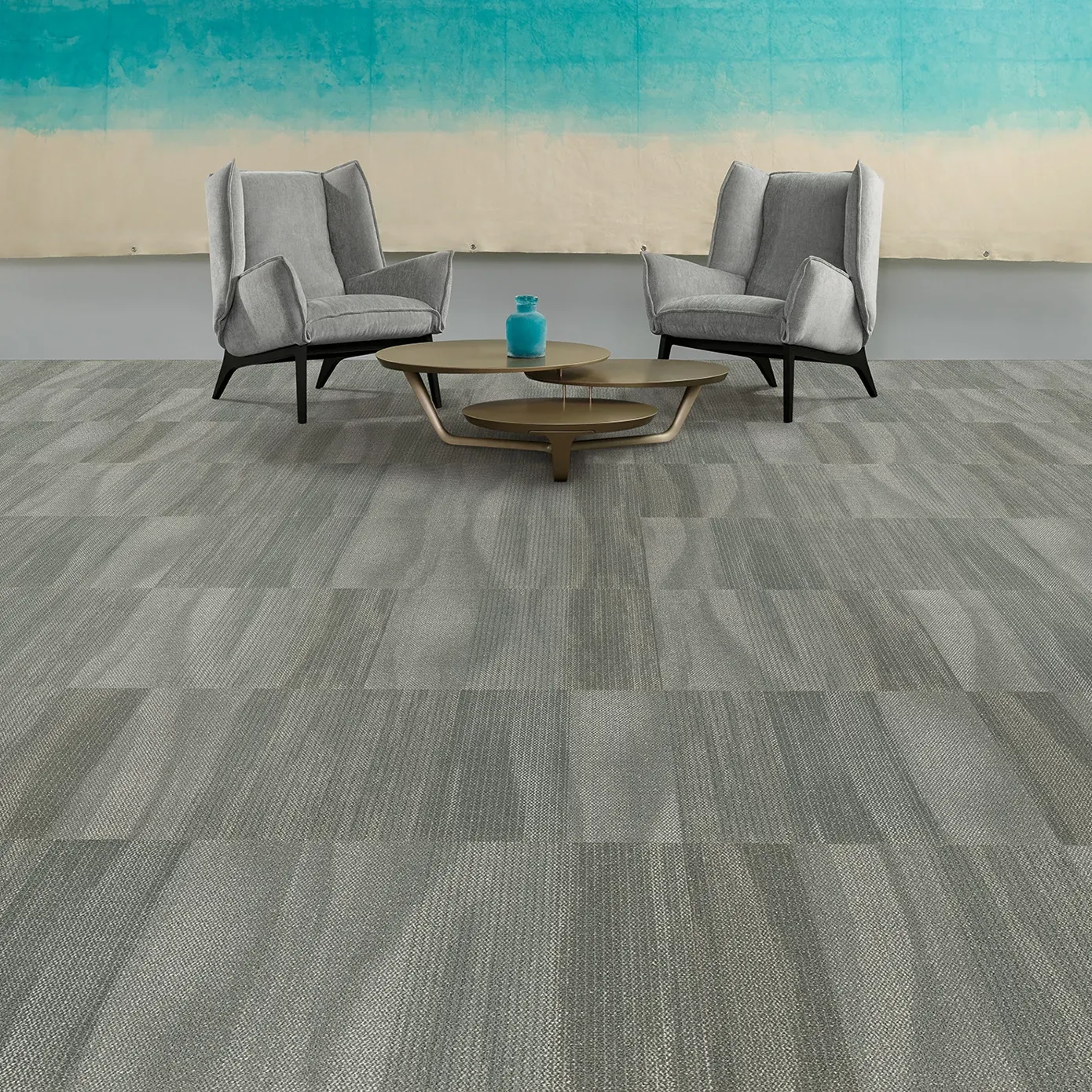 Modern lounge area with gray commercial carpet tile flooring, featuring two gray armchairs and a round coffee table against a blue and beige wall back