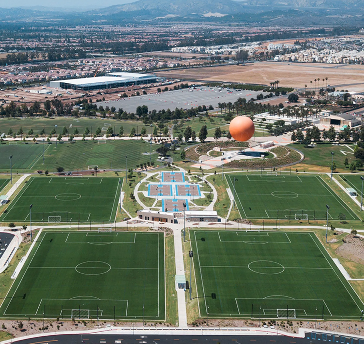 Aerial view of multiple soccer fields with artificial turf surrounded by a park and residential area