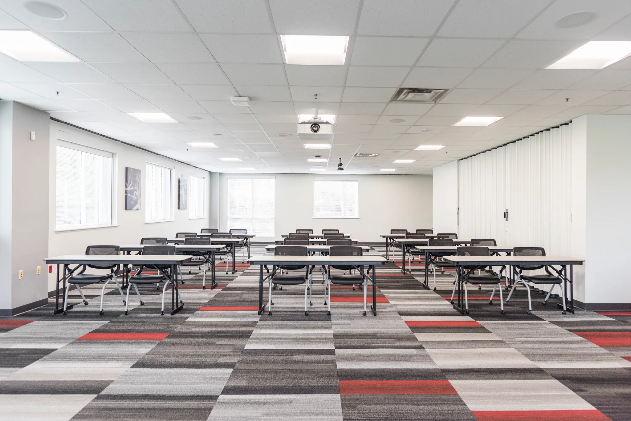 Modern education facility with commercial carpet tile flooring in shades of gray, black, white, and red, featuring rows of desks and chairs in a bright, spacious classroom setting