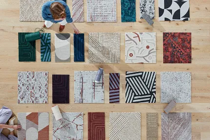 Carpet Tile Swatches Display on Wooden Floor Overhead view of diverse carpet tile swatches in various colors and patterns on a wooden floor with two people arranging them