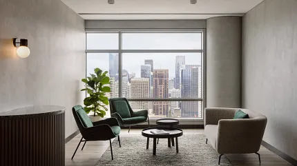 Contemporary Workplace Lounge with Hardwood Flooring and Cityscape View Modern office lounge with city view, featuring green chairs, a gray sofa, and a textured rug on hardwood flooring