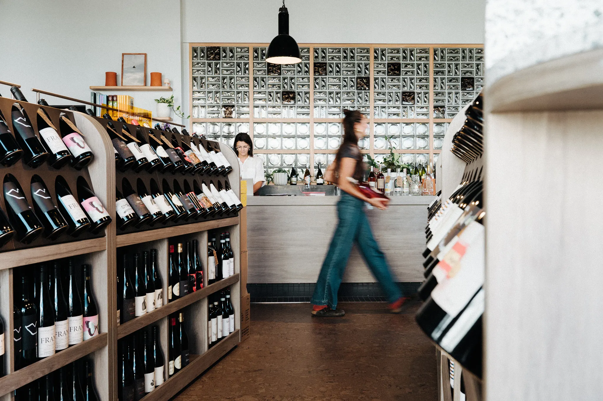 Retail store interior with wooden wine racks and a woman walking, featuring commercial flooring.