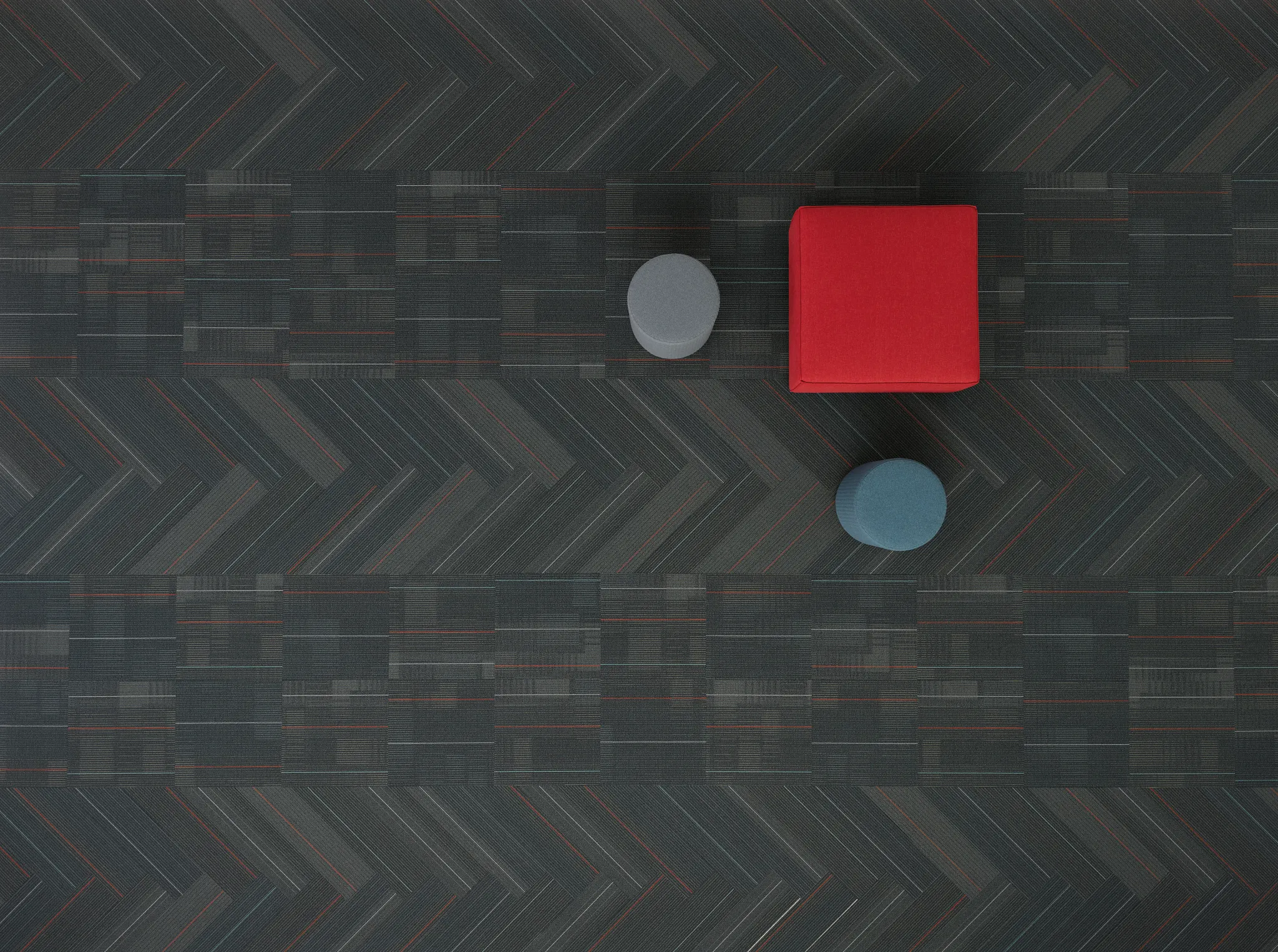 Vista superior de un diseño de piso contemporáneo con patrones oscuros en espiga y módulos cuadrados, complementado con elementos de mobiliario en tonos rojo, gris y azul.
