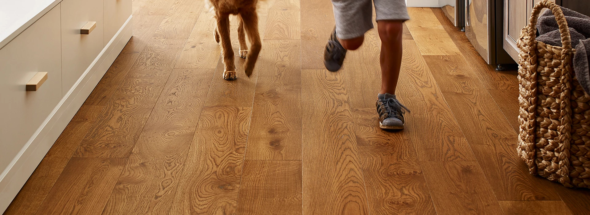 A boy and dog running through a kitchen with a hardwood floor