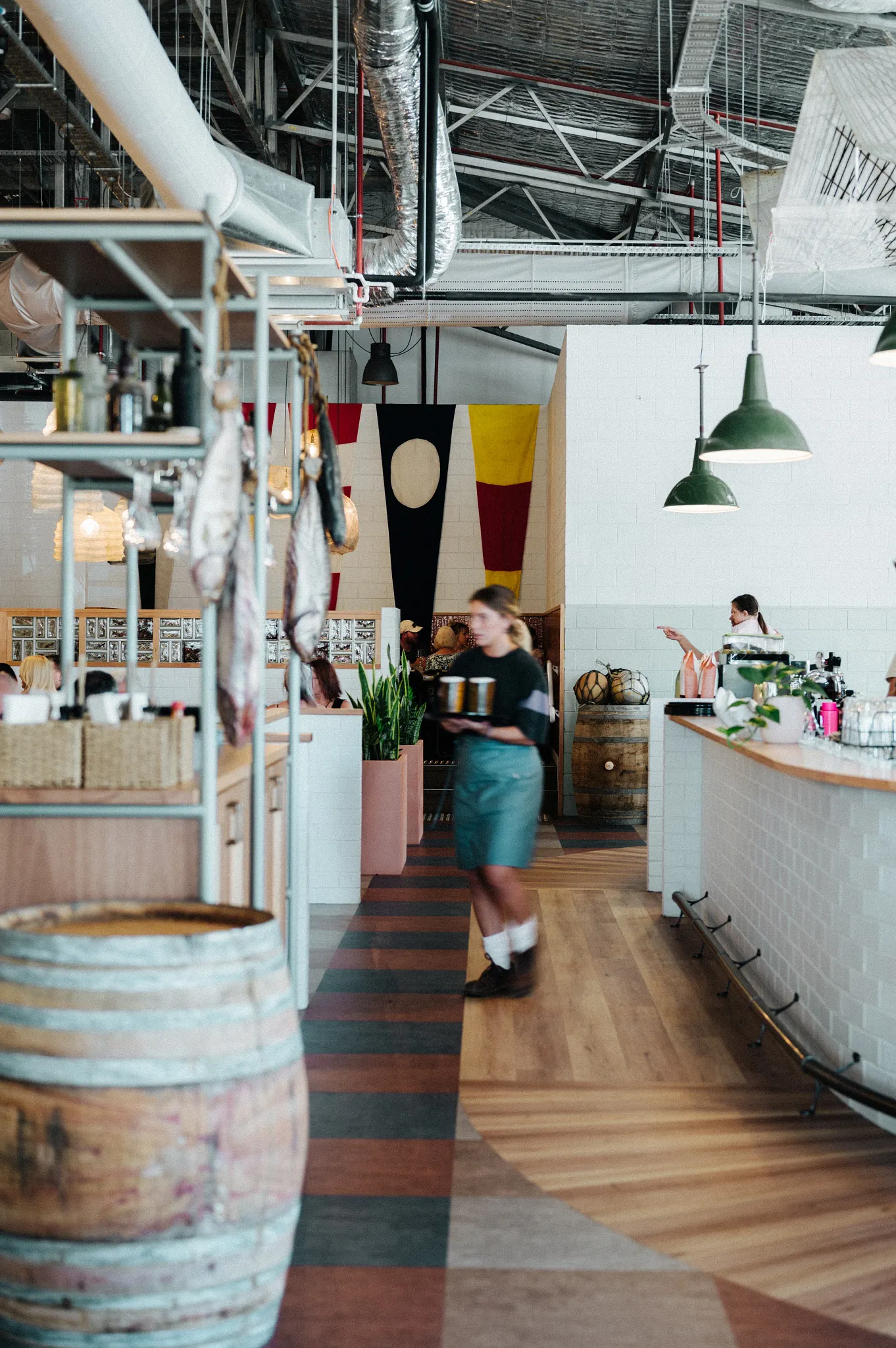 Modern restaurant interior with mixed wood and tile flooring, featuring industrial decor and vibrant wall hangings