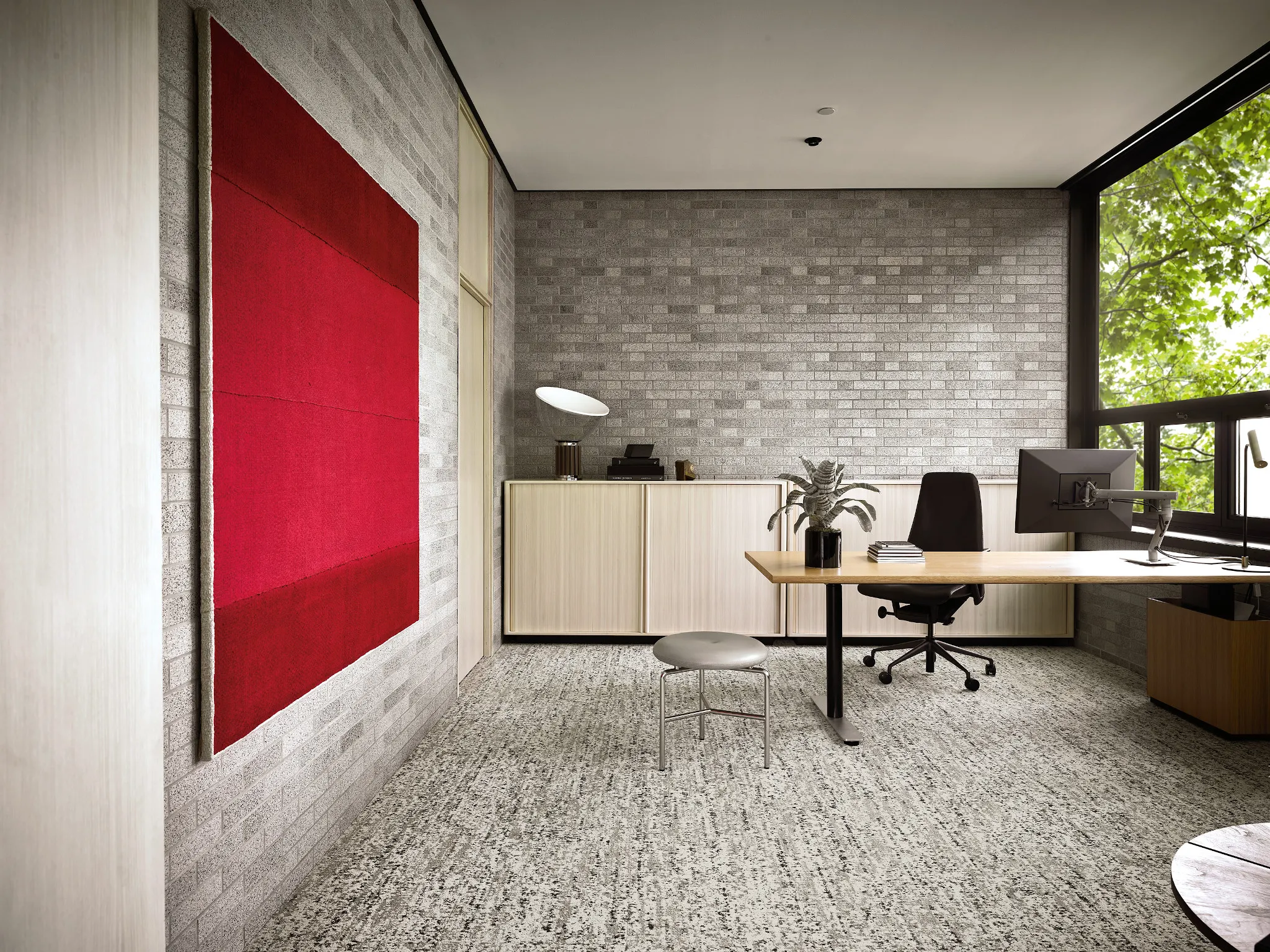Modern office space with large window, featuring a textured gray carpet and a vibrant red wall art
