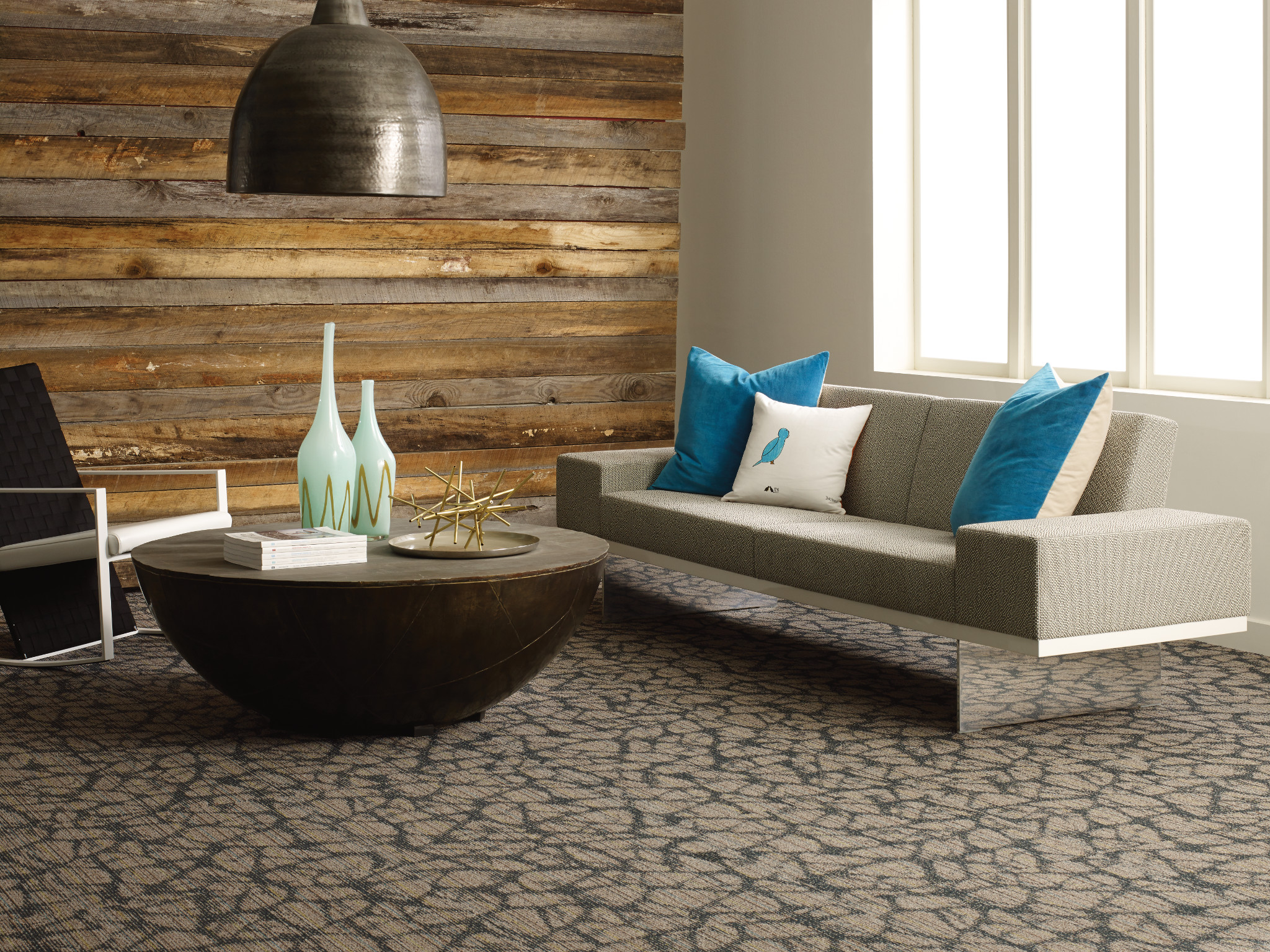 
  "Modern living room with textured carpet flooring, featuring a gray sofa with blue pillows and a round coffee table"
)
