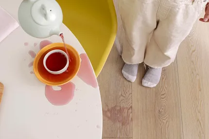 Waterproof Light Wood Look Vinyl Flooring - Durable and Easy to Clean Child standing on light wood look vinyl flooring with spilled tea on the floor, showcasing waterproof and durable features.