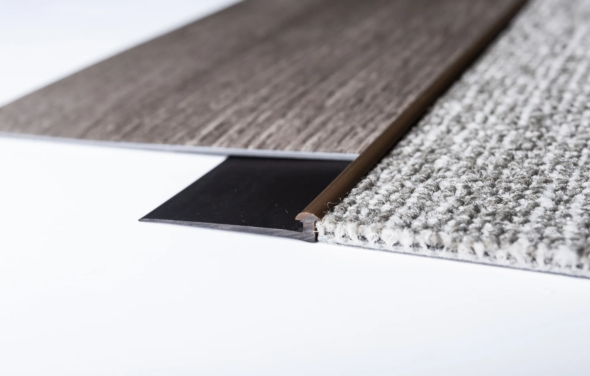 Close-up of flooring transition between gray commercial carpet tile and dark wood-look commercial LVT