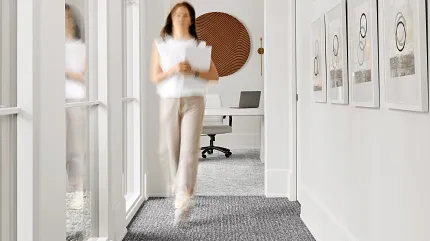 Contemporary hallway with gray commercial carpet tile flooring and wall art. Modern hallway with commercial carpet tile flooring in a neutral gray tone, featuring a woman walking and framed artwork on the walls