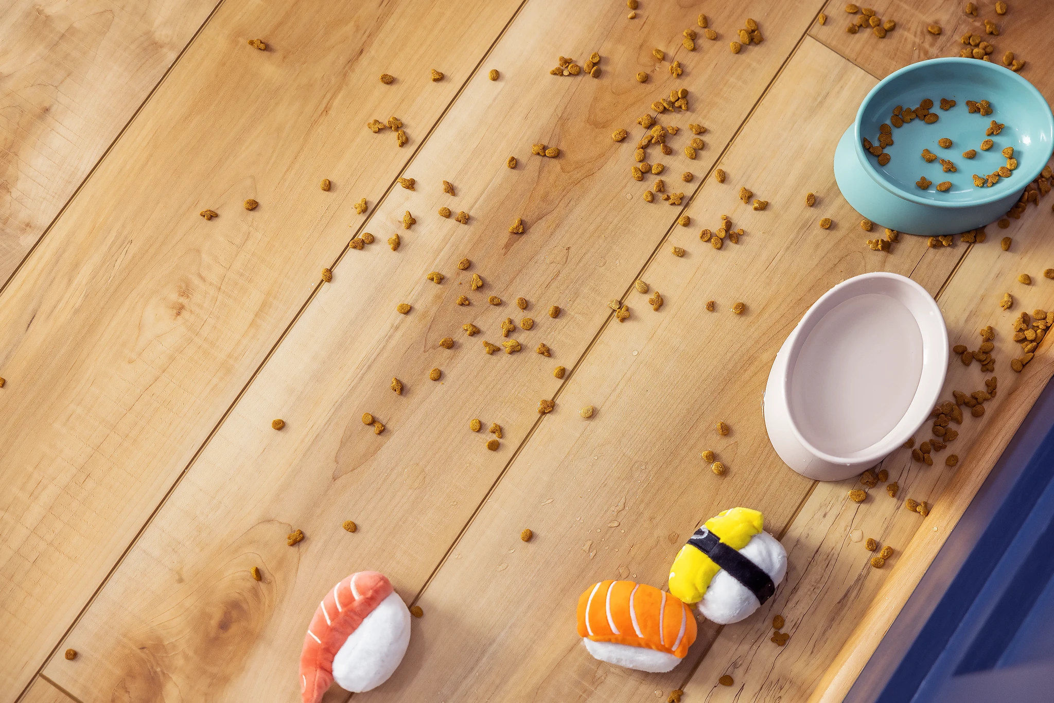 Light wood look luxury vinyl plank flooring with pet food bowls and toys scattered