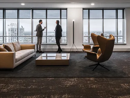 Contemporary office interior with commercial carpet flooring and city view Modern office space with large windows, two people conversing, and dark commercial carpet flooring