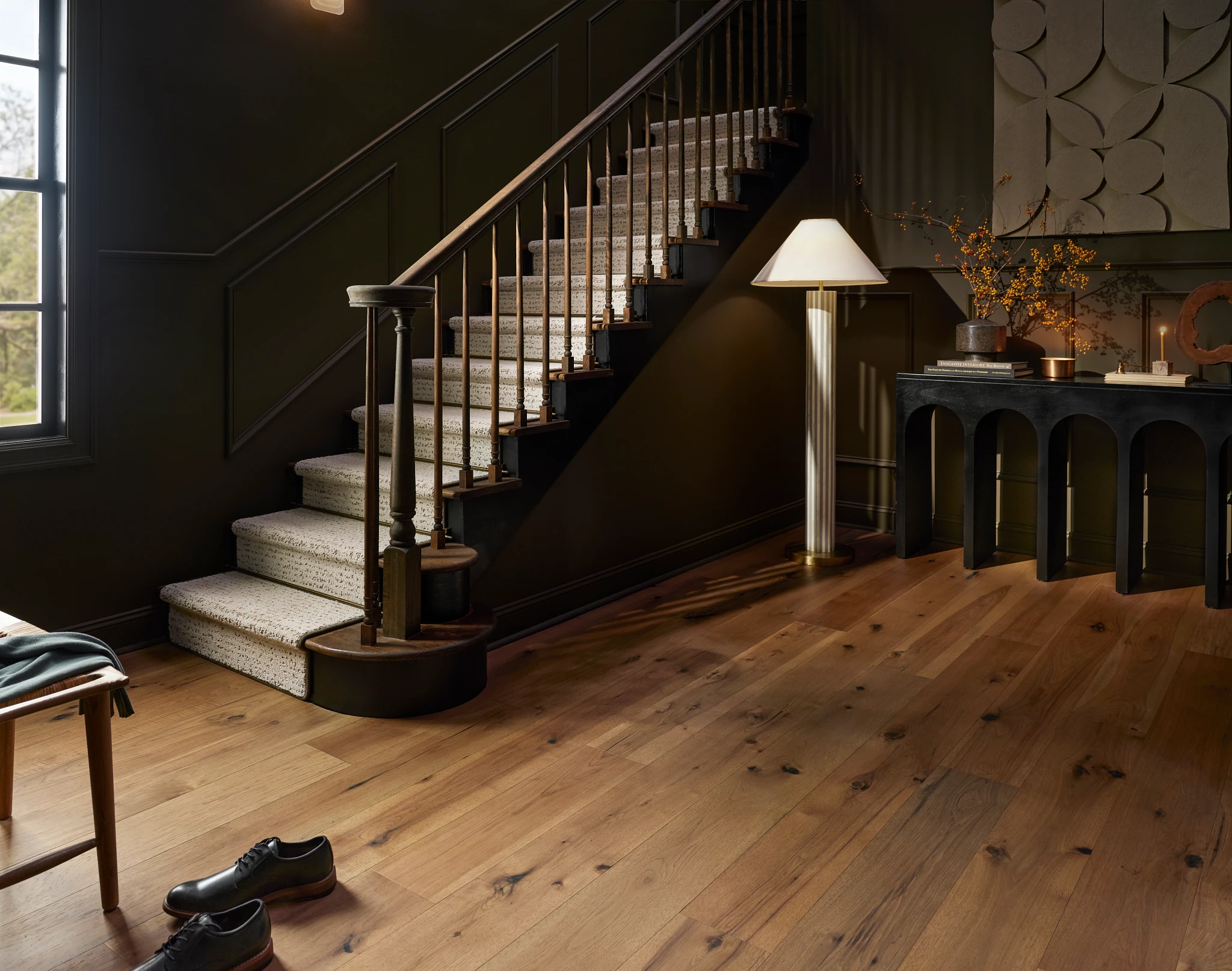 Elegant hardwood flooring in a stylish home entryway with a staircase and dark walls