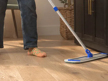 Easy-to-Maintain Light Wood Flooring for Everyday Comfort Person cleaning light wood flooring with mop and hard surface cleaner in a cozy home setting