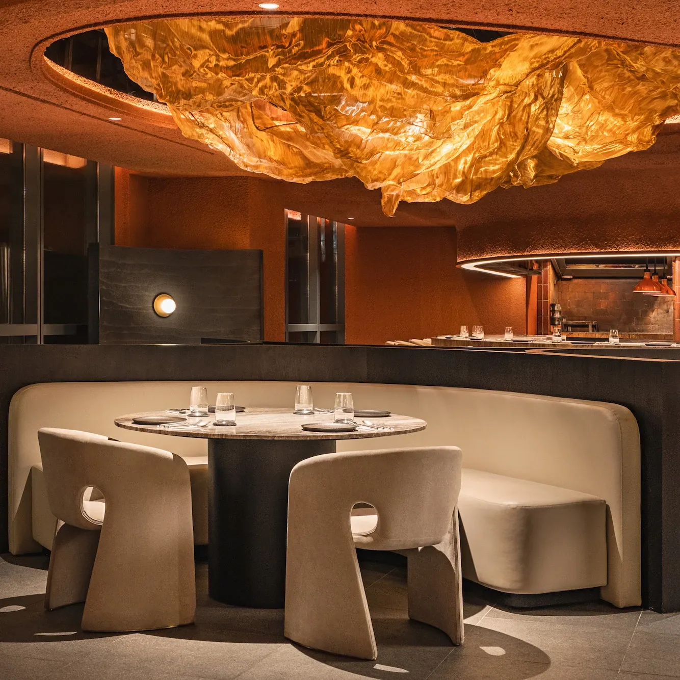 Elegant restaurant interior with modern beige chairs and a round table under a striking golden ceiling feature