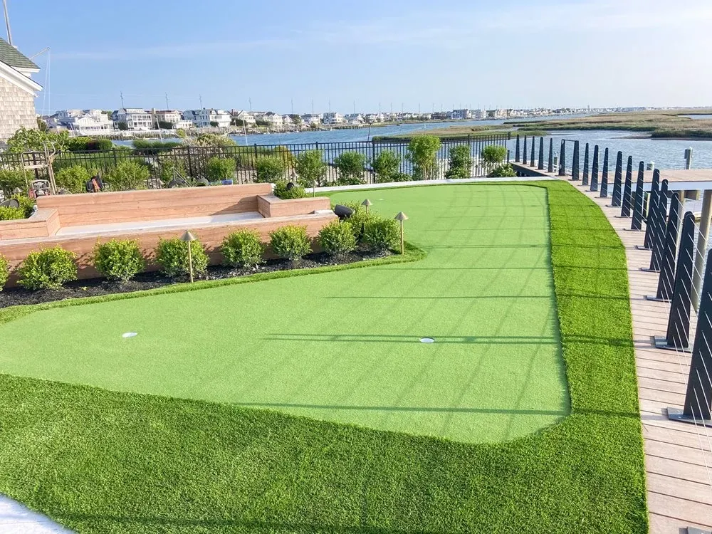Residential backyard putting green overlooking waterfront homes with elevated wood deck and artificial turf landscaping.