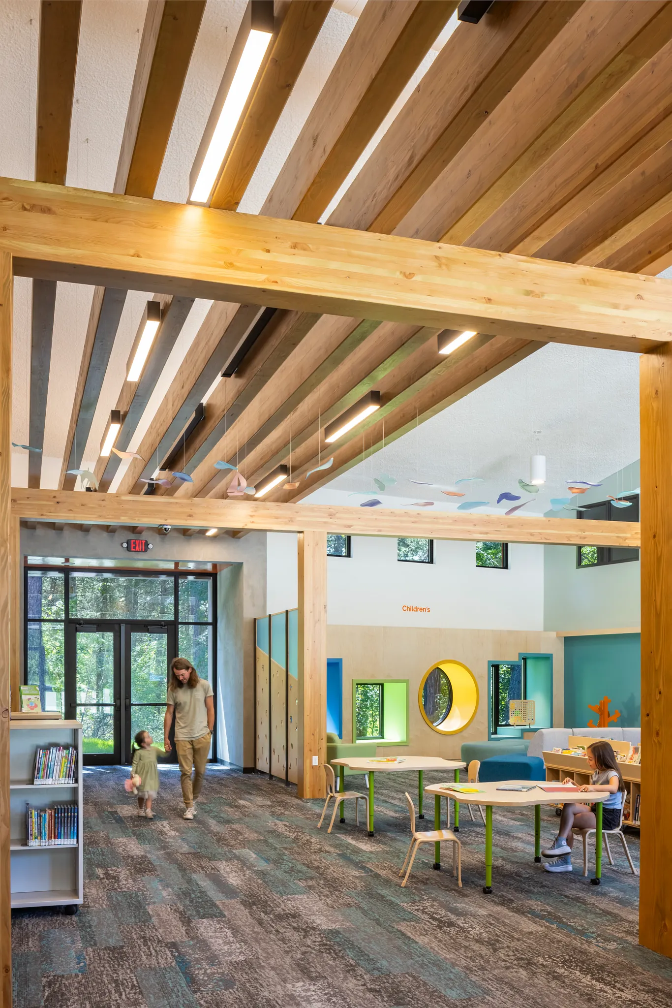 Education facility with commercial carpet tile flooring in shades of gray and teal, featuring wooden beams and colorful children's area with tables and chairs