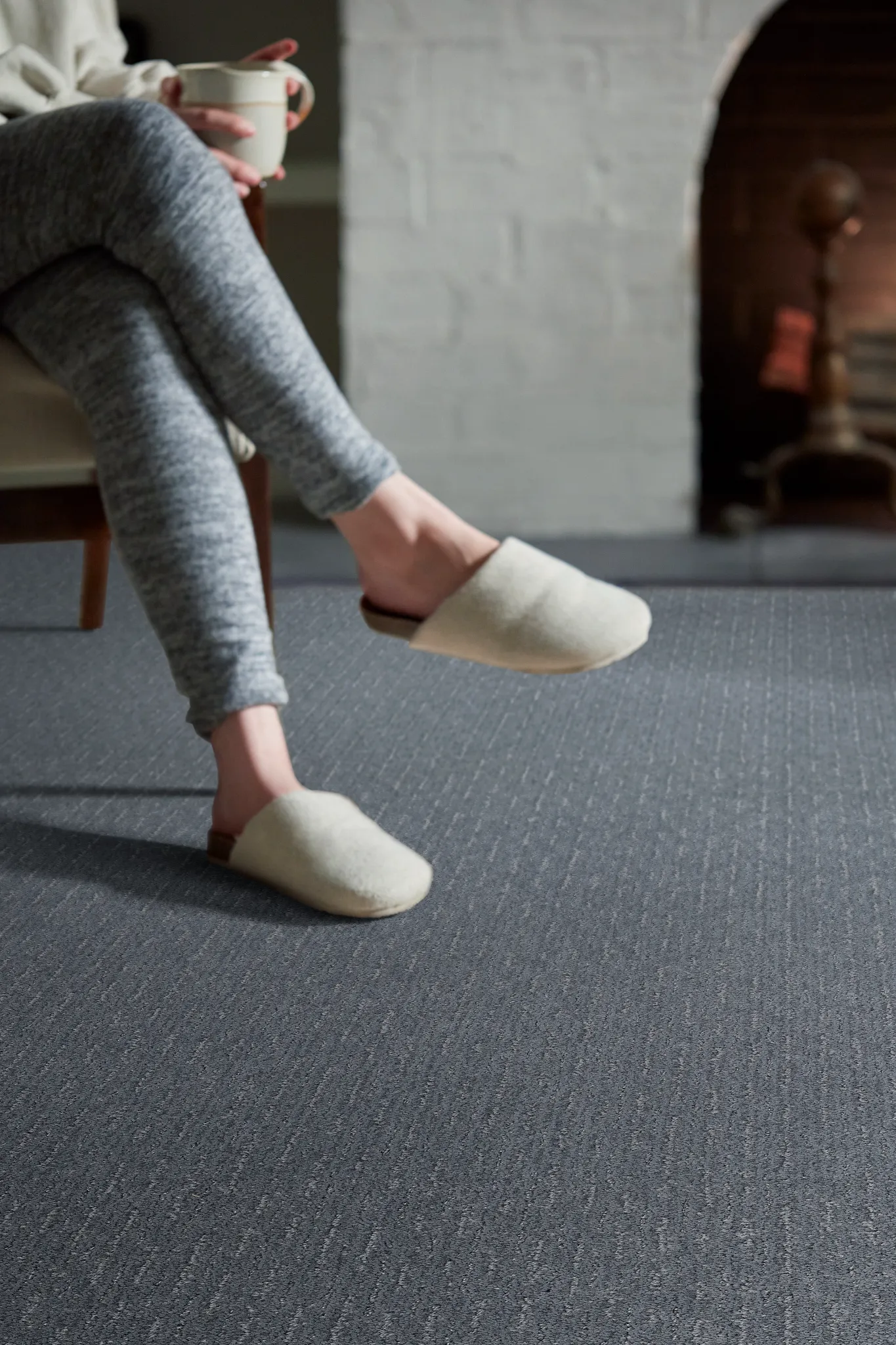 Cozy living room scene with a person in slippers enjoying a warm drink on durable, easy-to-maintain dark gray carpet