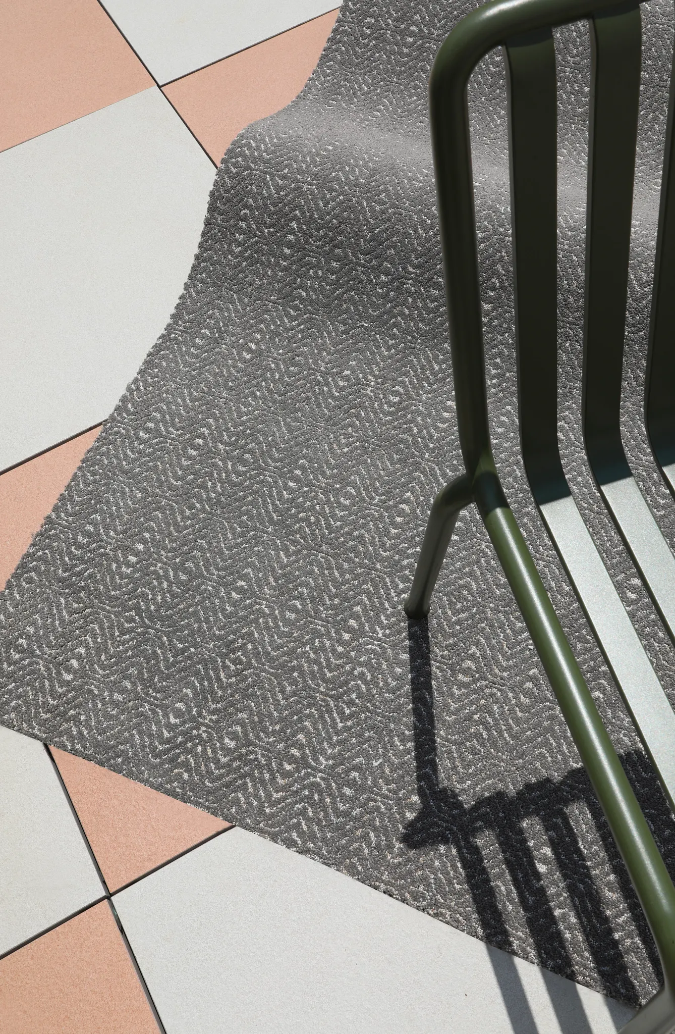 Gray patterned carpet with a textured design next to a green metal chair on a tiled floor