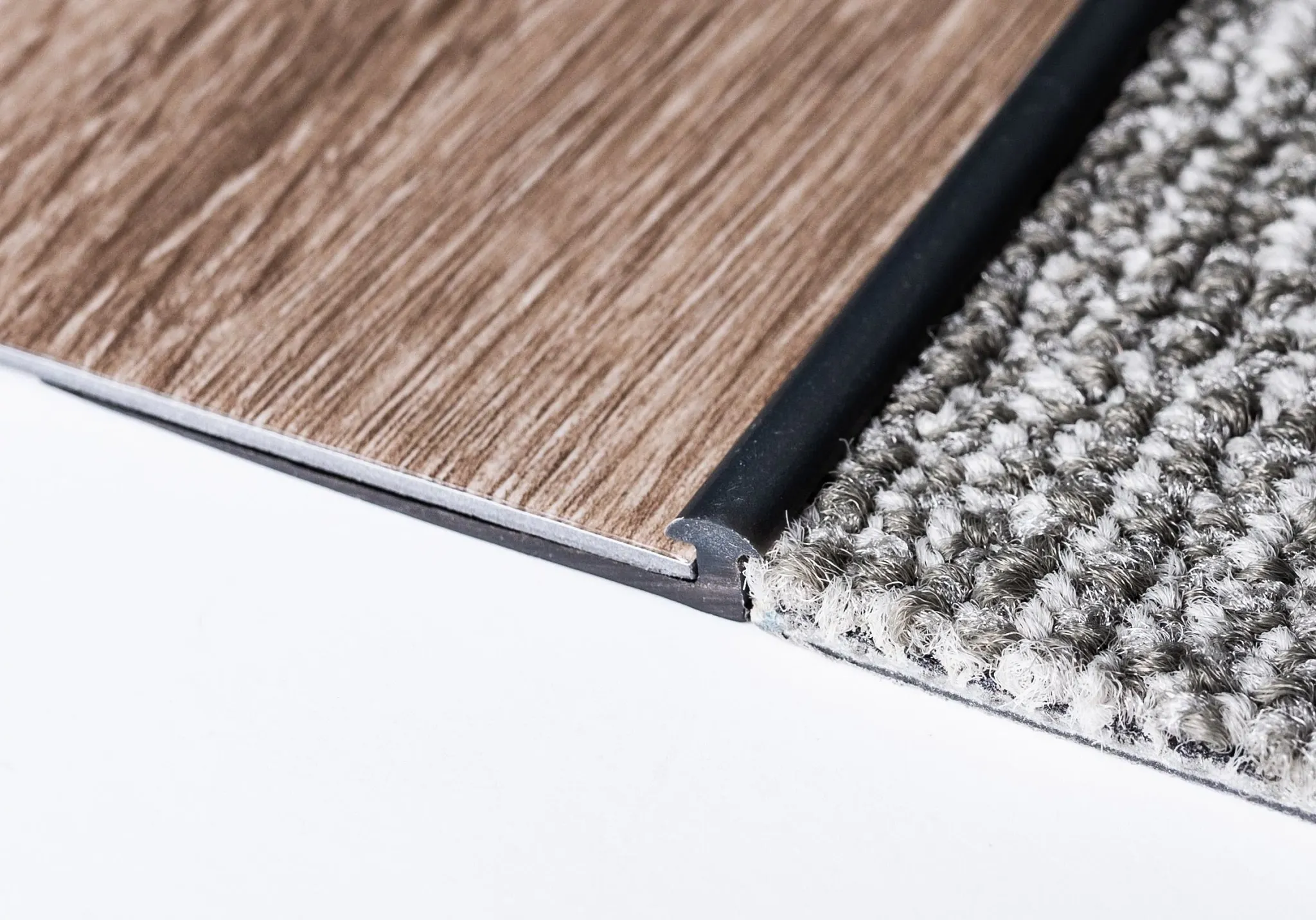 Close-up of flooring transition between wood-look vinyl and gray textured carpet