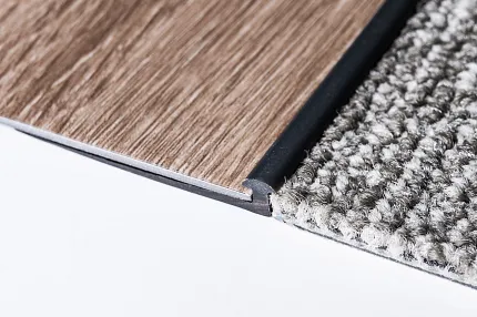 Flooring Transition Detail - Wood-Look Vinyl and Gray Carpet Close-up of flooring transition between wood-look vinyl and gray textured carpet