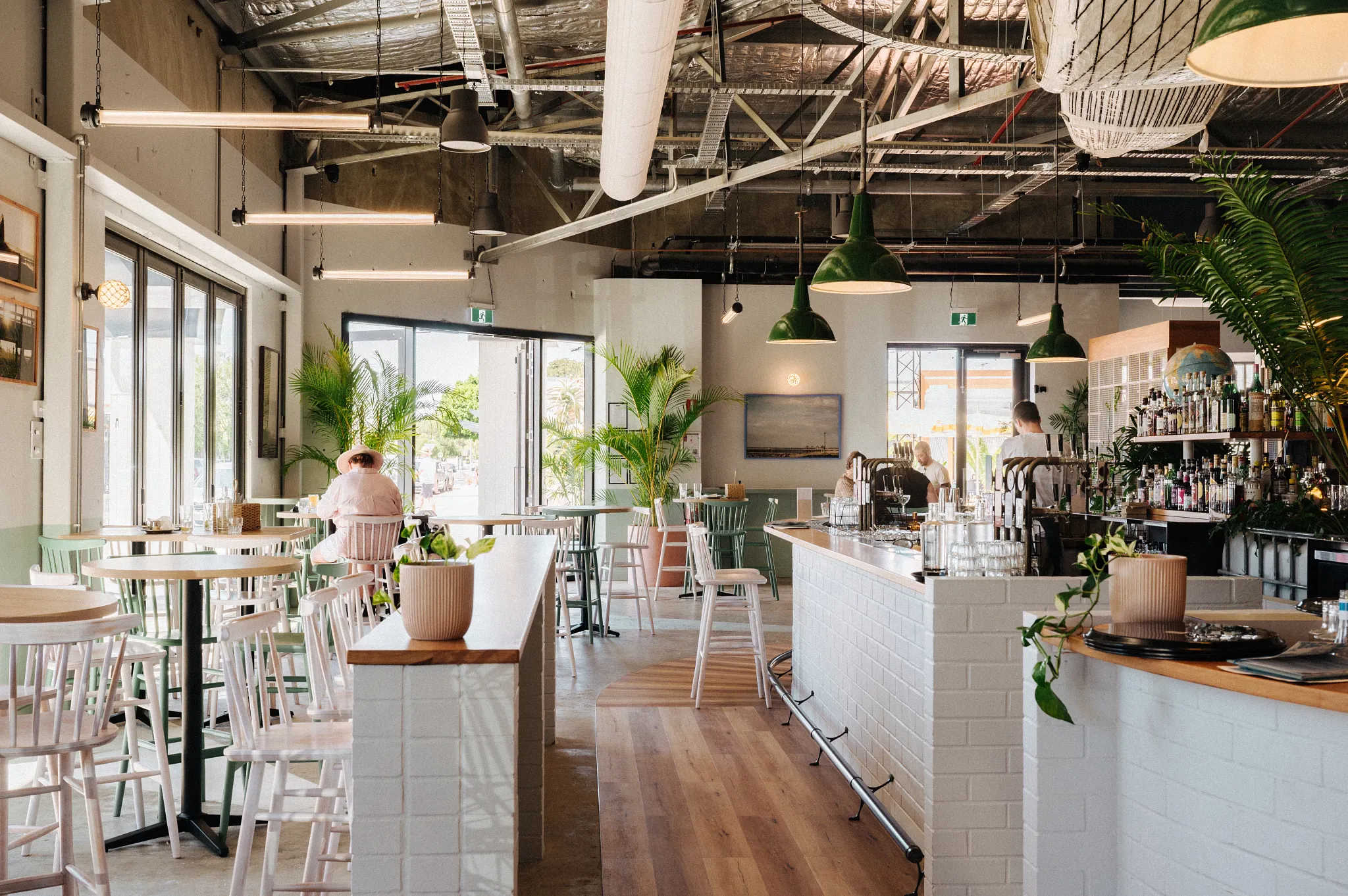 Interior de restaurante moderno con piso de madera, mostradores de ladrillo blanco y lámparas colgantes verdes