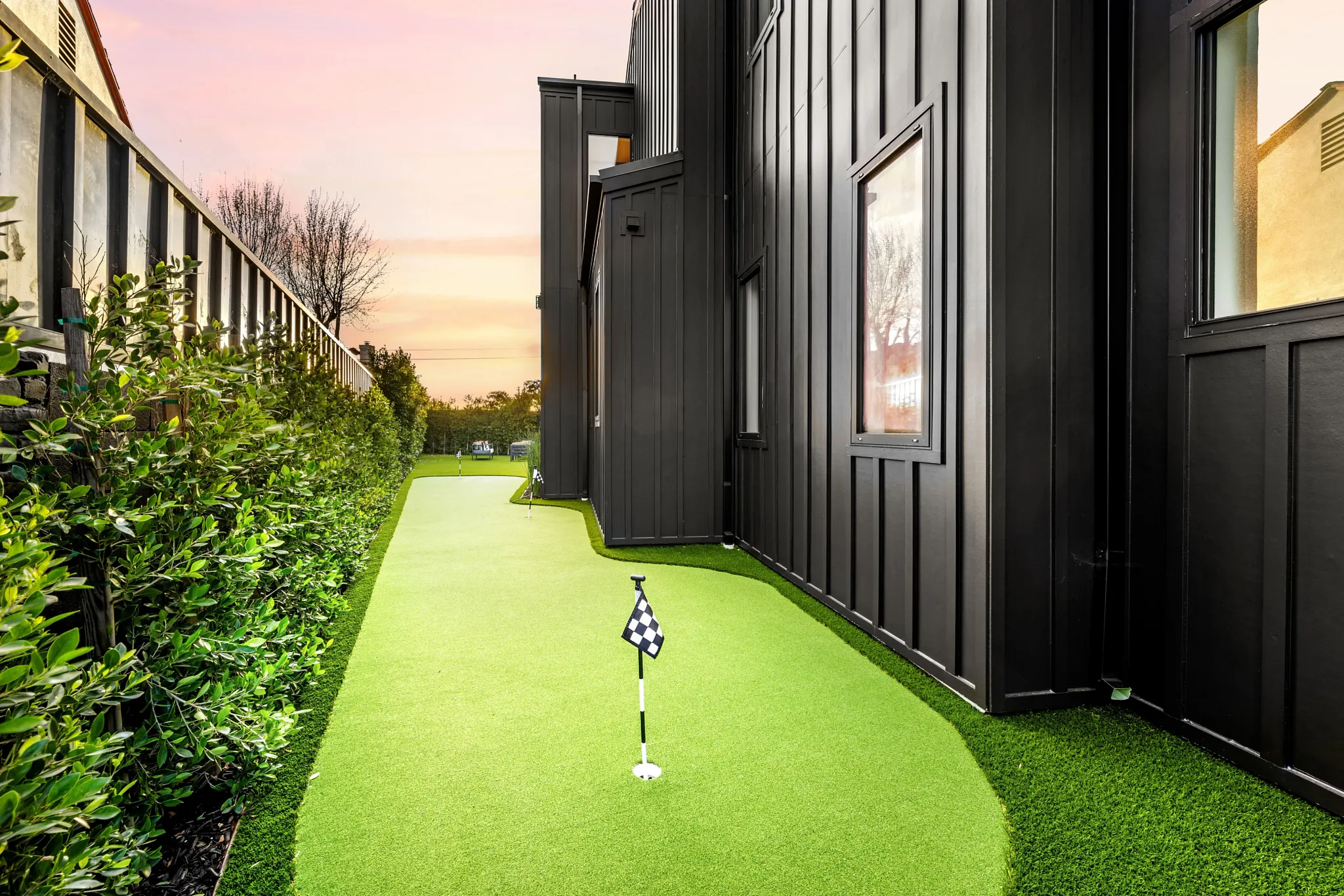 Narrow artificial turf putting green alongside modern black exterior home