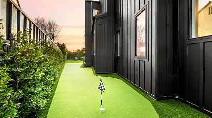 Backyard synthetic grass putting green beside contemporary house Narrow artificial turf putting green alongside modern black exterior home