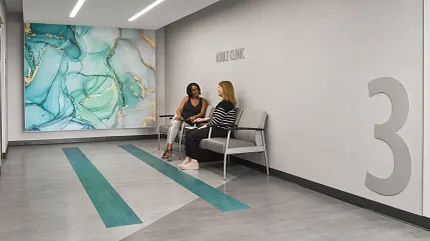 Modern Healthcare Facility Waiting Area with Teal and Gray Flooring Healthcare facility waiting area with modern design featuring teal and gray flooring, abstract wall art, and two women seated on chairs