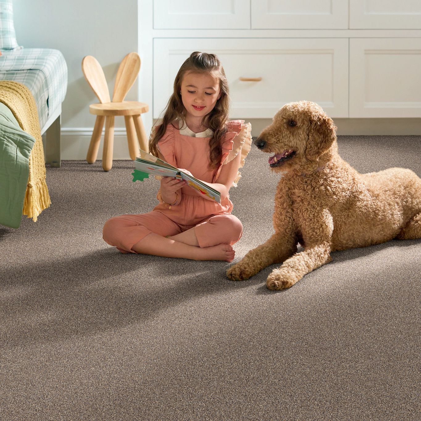 A girl and her dog sit on her bedroom carpet reading a book.