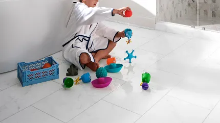 White Stone Look Luxury Vinyl Tile Flooring - 24x12 inch - Coretec Residential WPC Child playing with toys on white stone look luxury vinyl tile flooring in a bathroom