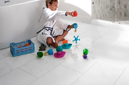 White Stone Look Luxury Vinyl Tile Flooring - 24x12 inch - Coretec Residential WPC Child playing with toys on white stone look luxury vinyl tile flooring in a bathroom