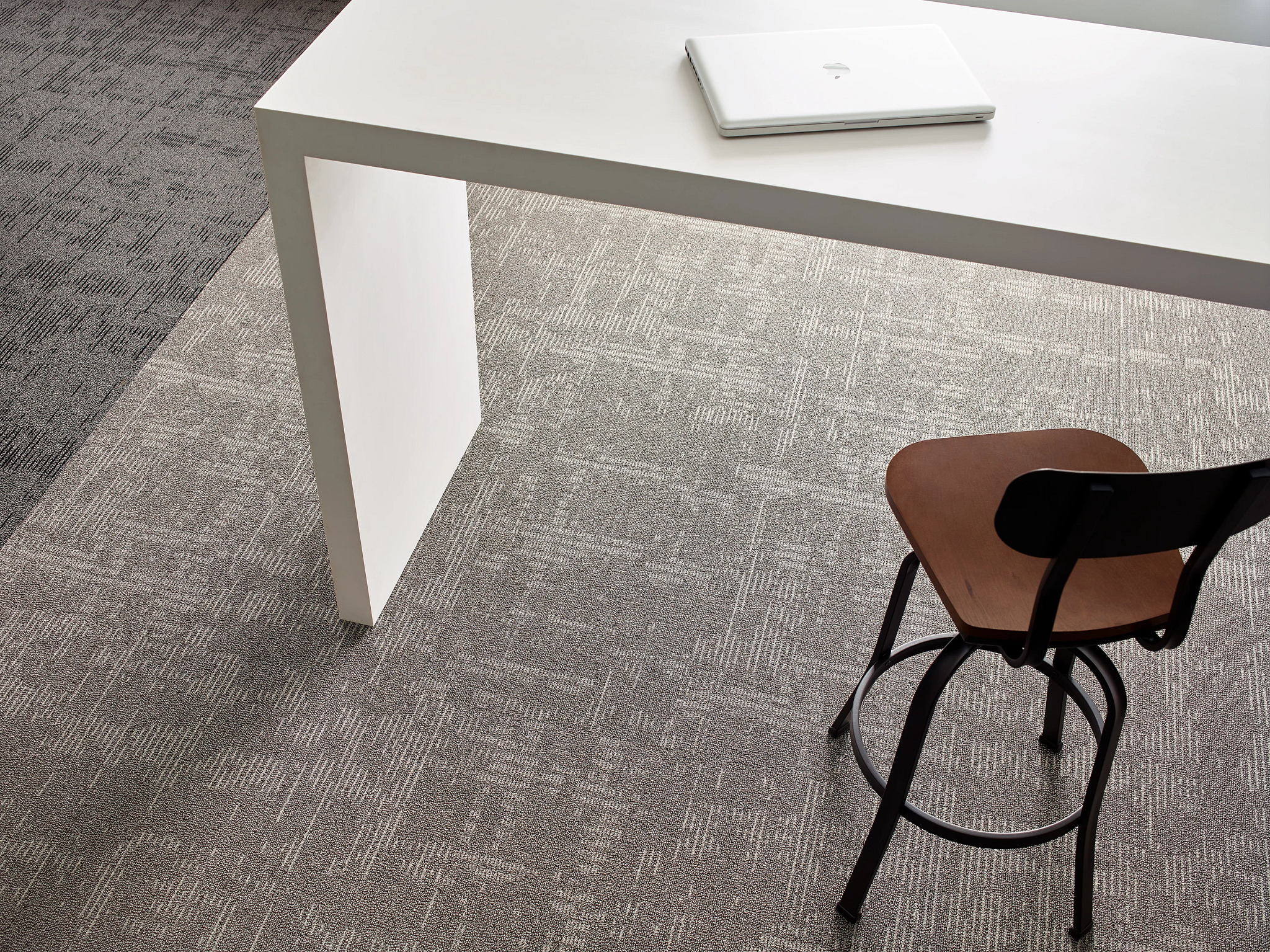 
  "Modern office space with a white desk and chair on gray patterned commercial carpet"
)
