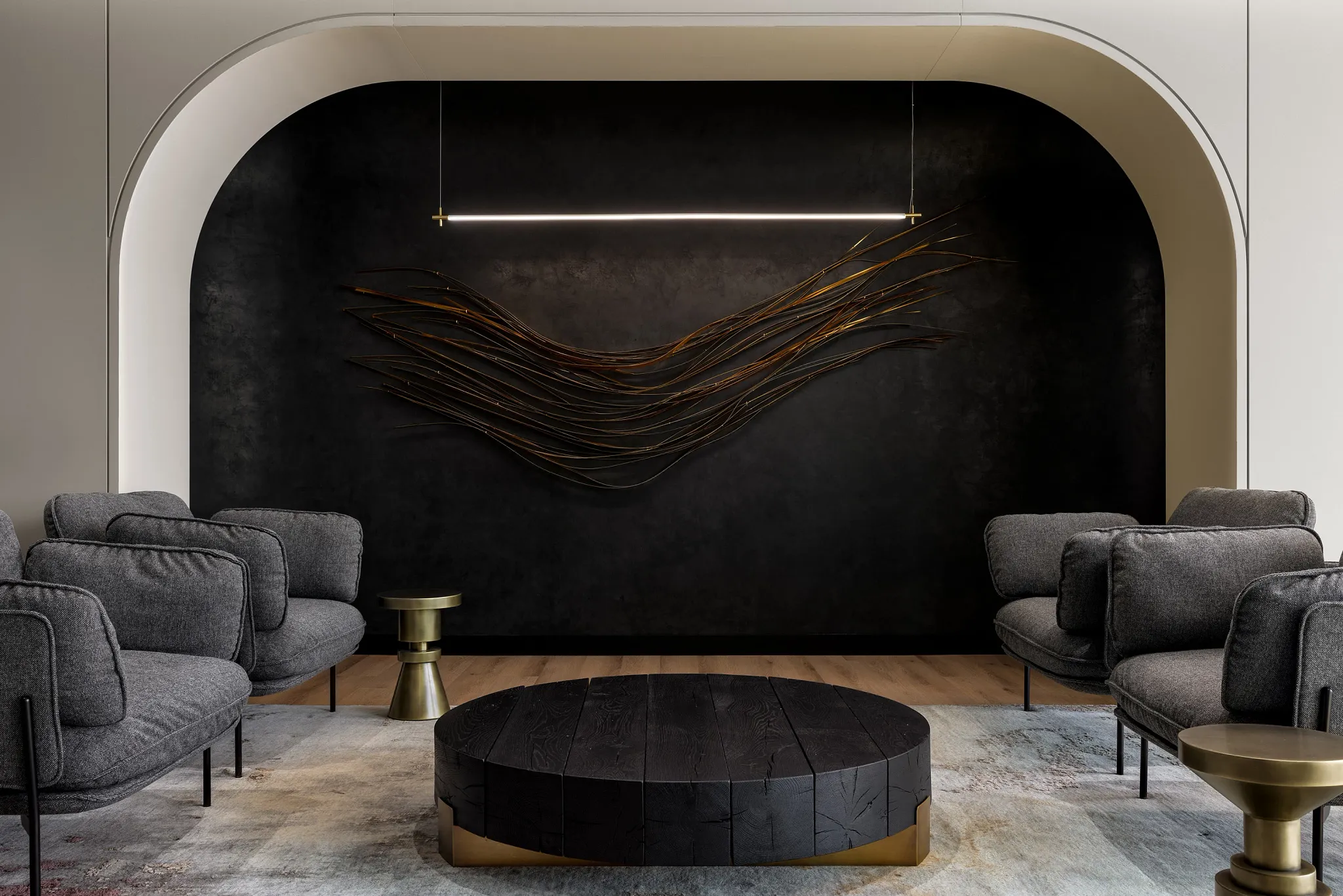 Modern workplace lounge with dark wood flooring, gray upholstered chairs, and a black circular coffee table