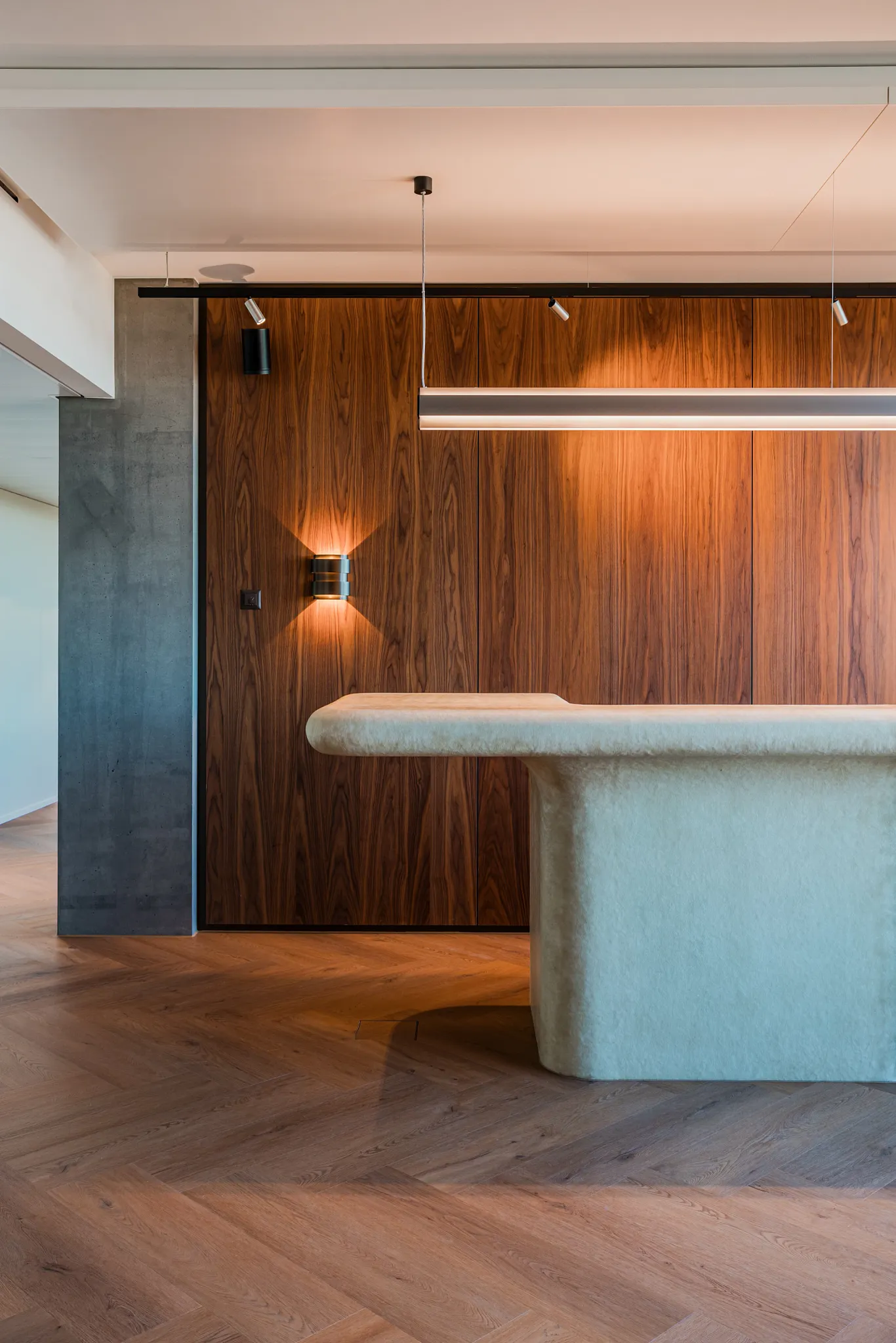 Modern reception desk with designer lighting, rich walnut storage room and rich wood herringbone floors