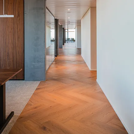 Open office hallway with wood herringbone Coretec floors in rich tones with
