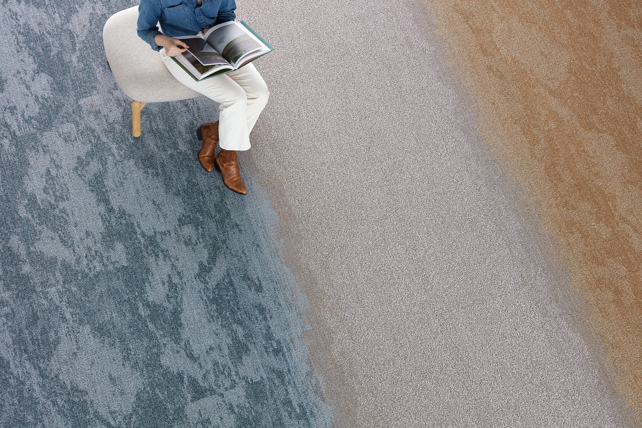Overhead view of a person sitting on a chair reading a book on a multi-colored carpet with blue, gray, and beige sections