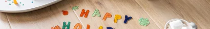 Light Wood Look Luxury Vinyl Plank Flooring - Holiday Scene Child decorating gingerbread houses on light wood look luxury vinyl plank flooring with "Happy Holidays" letters and a mug of hot chocolate