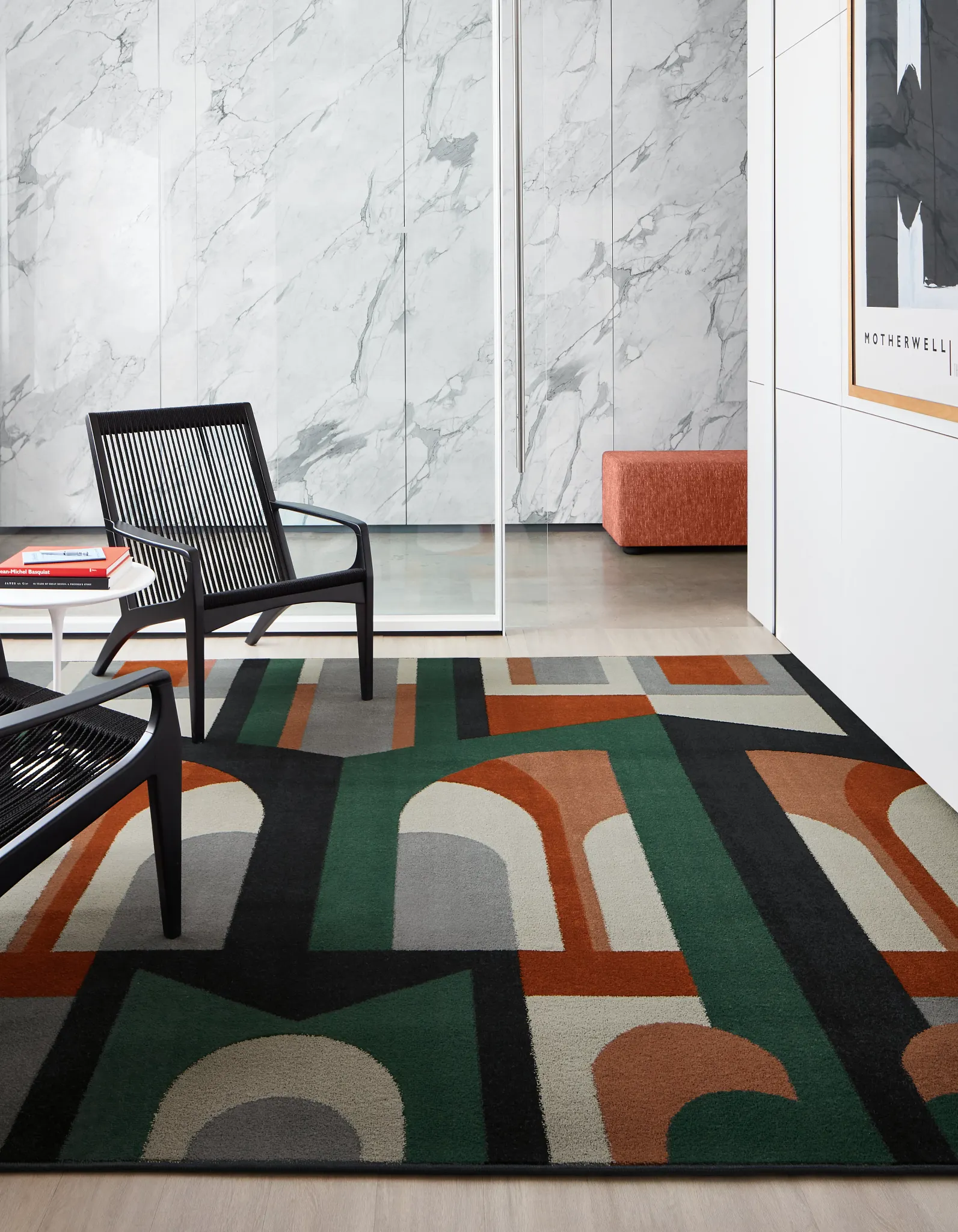 Modern office space with abstract patterned commercial carpet tile in black, green, orange, and gray, featuring black chairs and marble walls